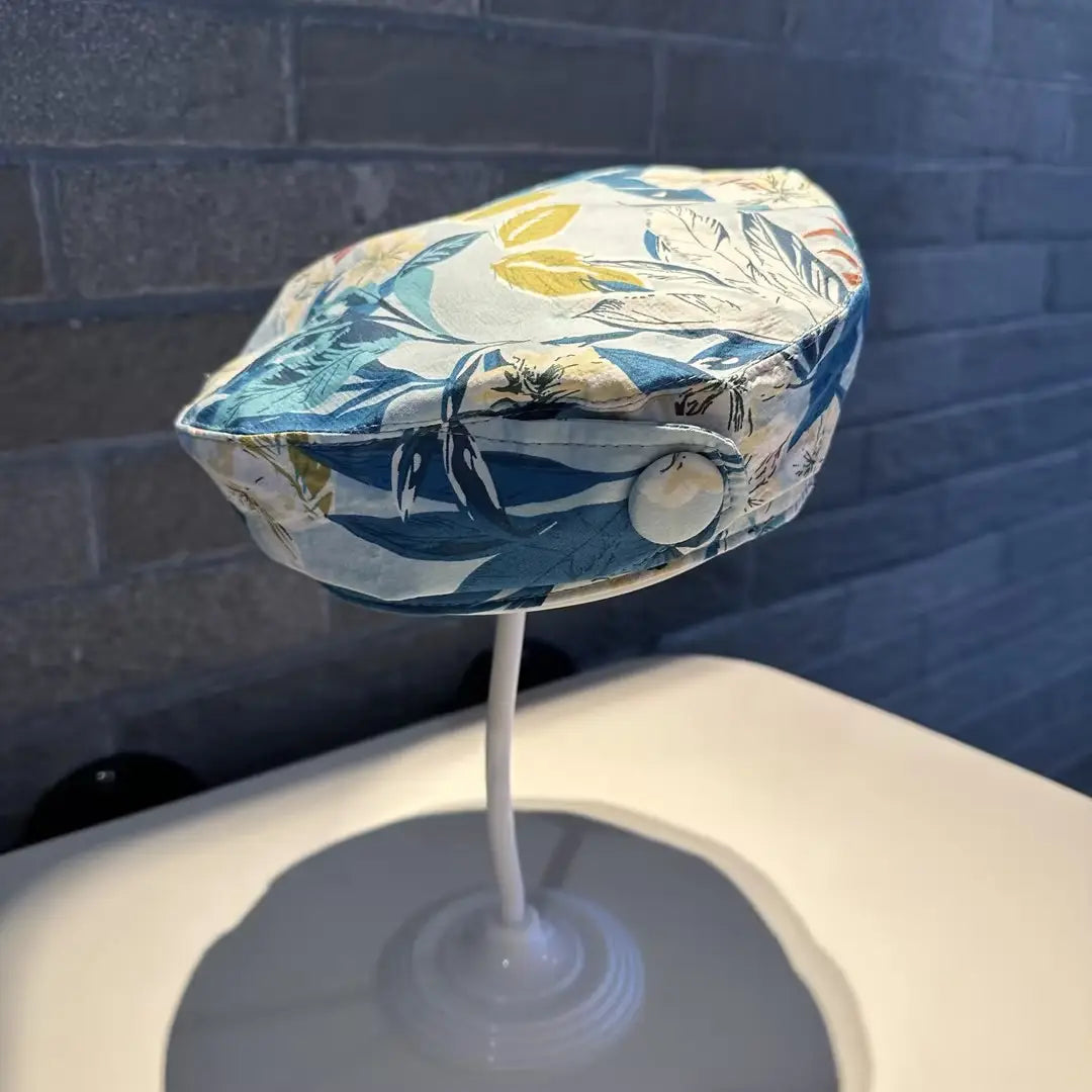 A stylish printed Korean style fashion cap in blue and white with a floral pattern, soft fabric texture, and decorative button closure.