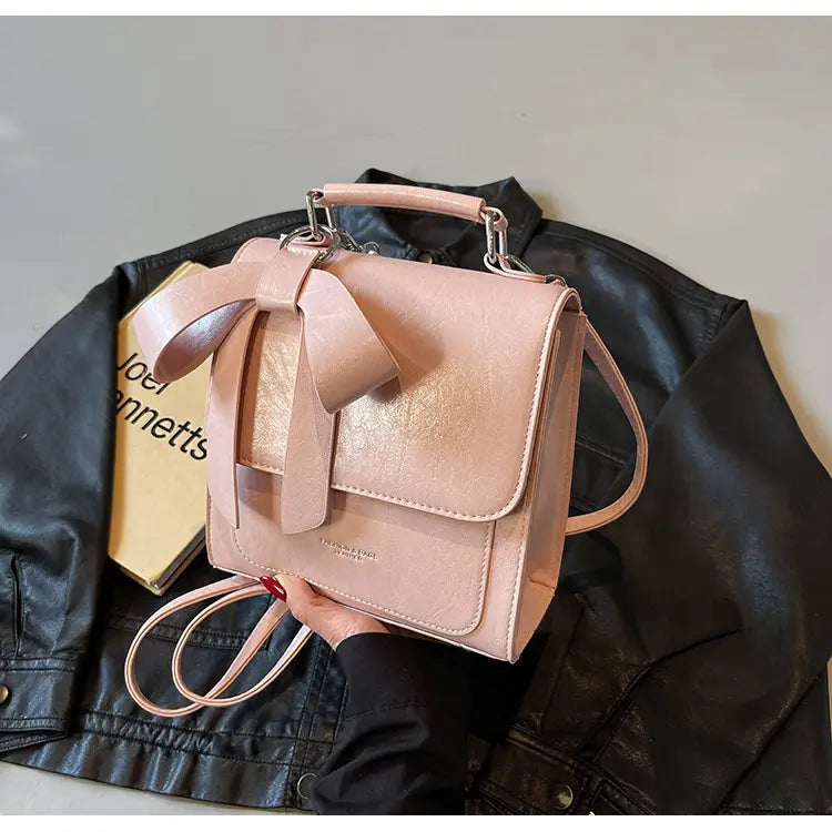 Blassrosa Umhängetasche aus Kunstleder mit auffälliger Vorder-Schleife und silberfarbenen Beschlägen, gestaltet als modische Handtasche.