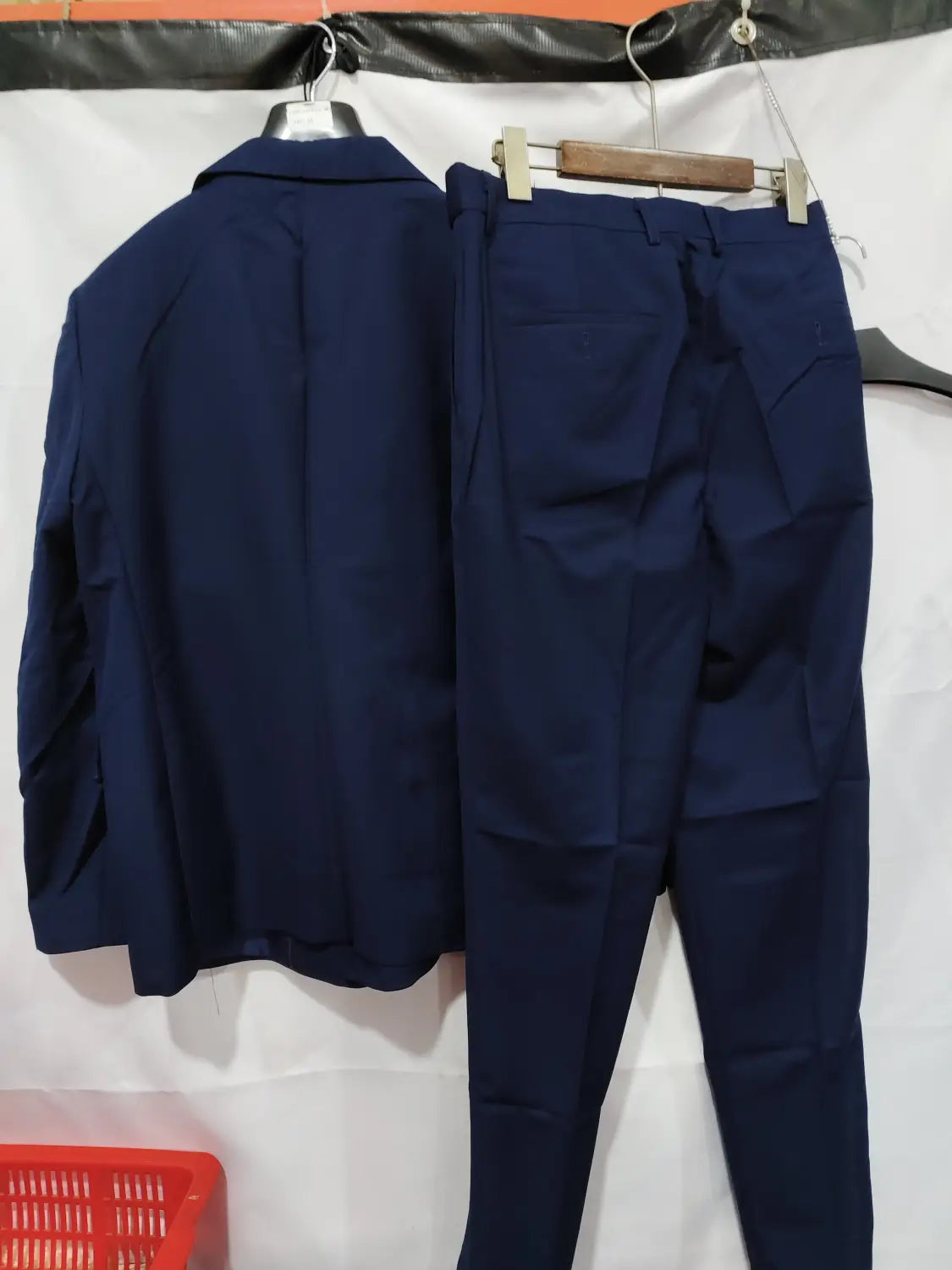 Veste de costume homme non repassable à double boutonnage bleu marine sur mesure, avec boutons dorés et pantalons assortis, suspendue sur des cintres.