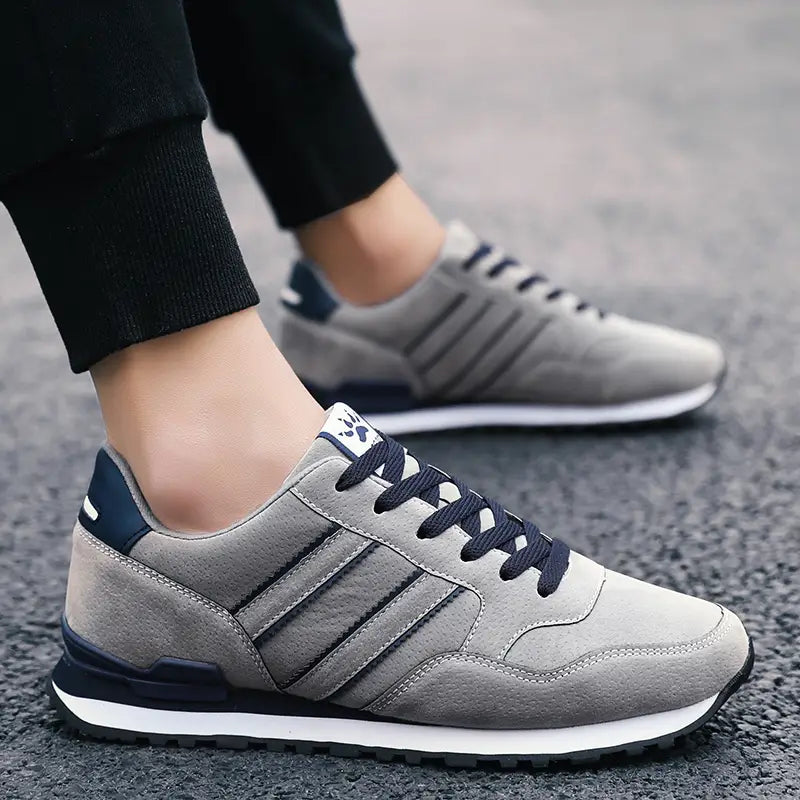 Baskets de mode athlétiques en daim pour hommes en gris, avec des touches de bleu marine et trois bandes parallèles sur le côté.