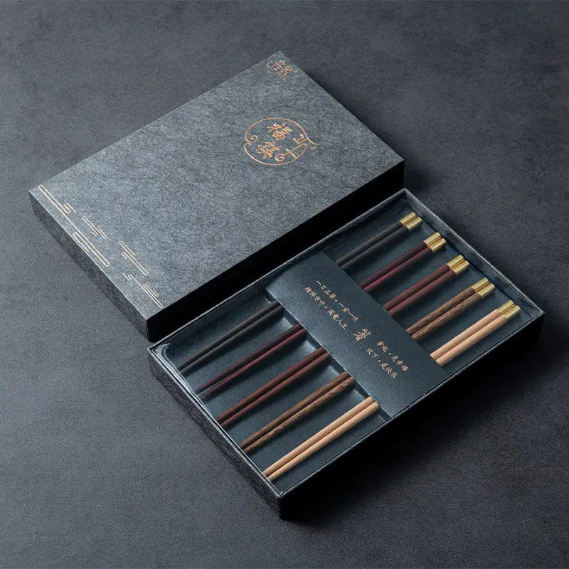 Set aus fünf Paar eleganten hölzernen Essstäbchen mit goldfarbenen Spitzen in einer anspruchsvollen dunkelgrauen Geschenkbox mit Elementen eines traditionellen chinesischen Designs.