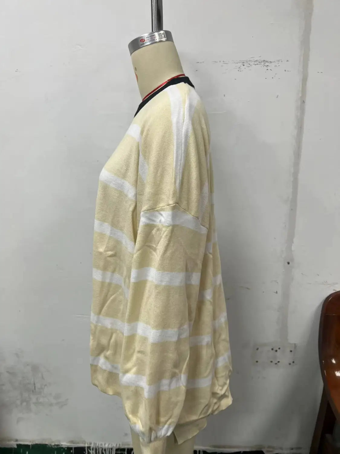 Women’s oversized split color striped knit sweater displayed on a mannequin featuring pale yellow and white horizontal stripes with a black collar and long sleeves.