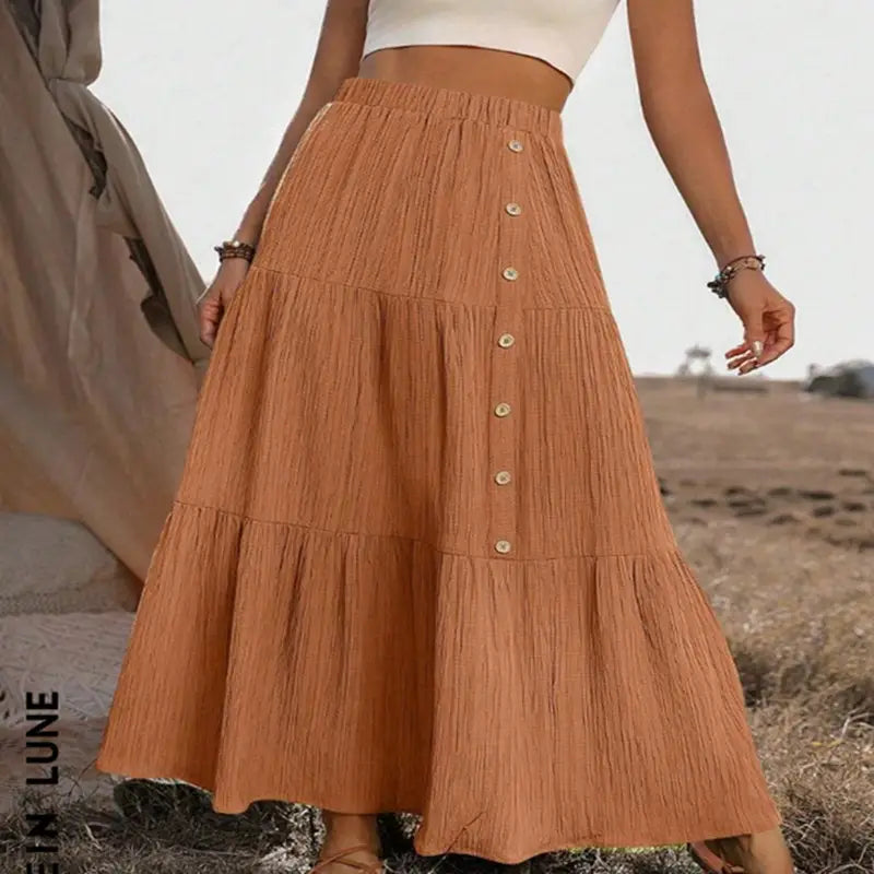A flowing tiered orange maxi skirt with a gathered waist and button closures made of lightweight fabric for casual wear.