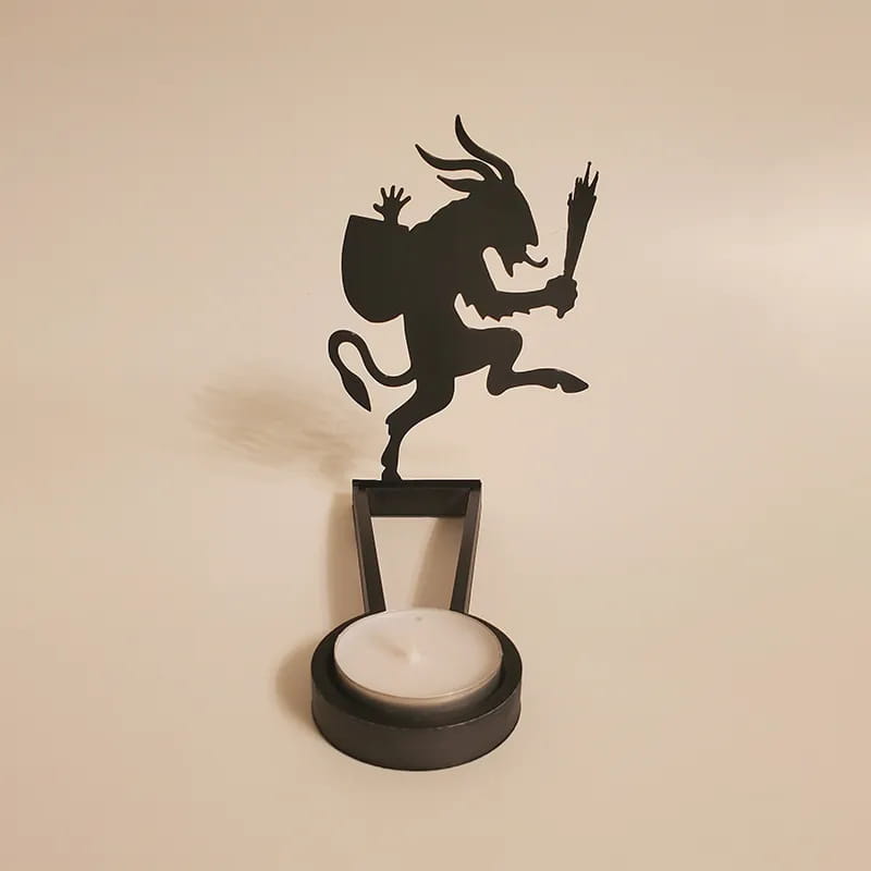 Black metal devil figurine atop a cylindrical tealight holder in a Halloween bat candle holder black metal shadow decor.