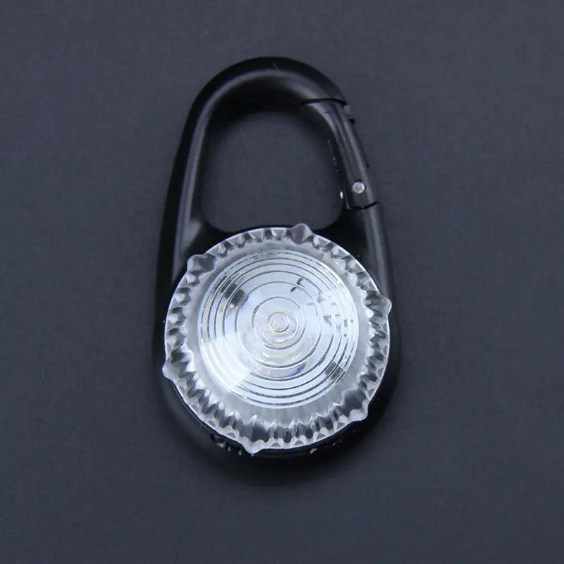 Pince de sécurité pour collier de chien à DEL de type mousqueton en carabine noir, avec une lentille texturée transparente présentant des stries circulaires concentriques.