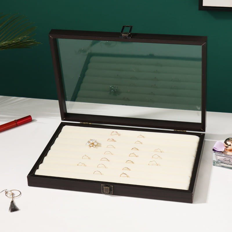 Rosewood jewelry display box with a clear glass lid and white foam inserts holding multiple rings in a dark brown wooden finish.