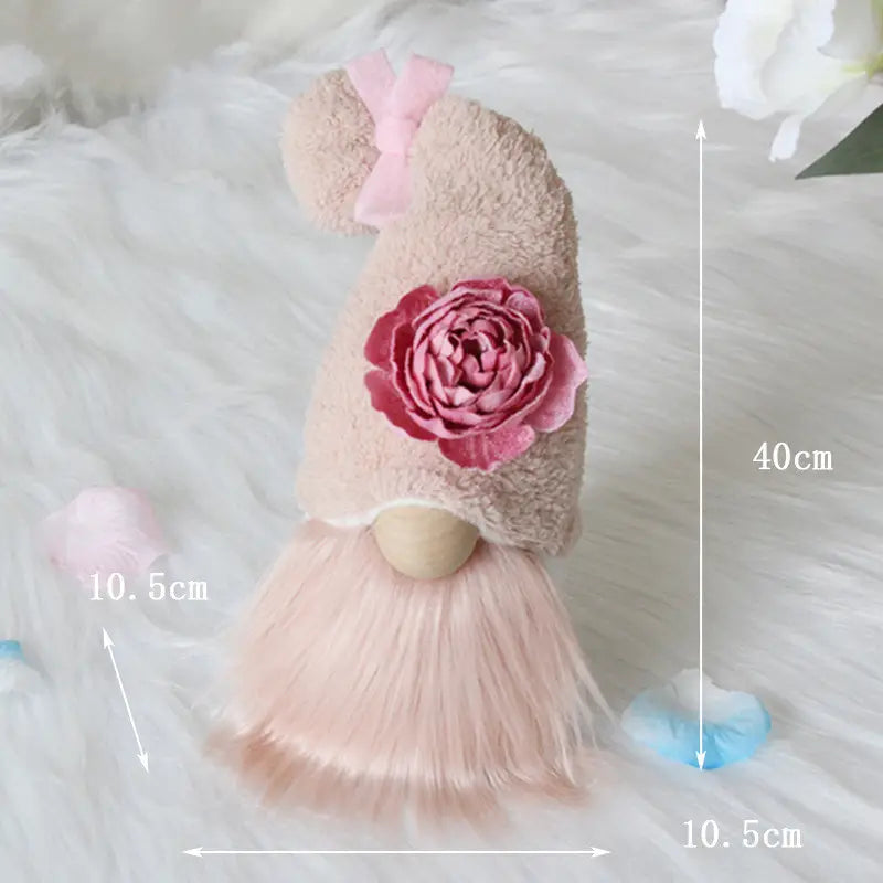 A soft pink plush gnome doll desktop ornament featuring a fuzzy hat adorned with a large rose and bow and a fluffy skirt.