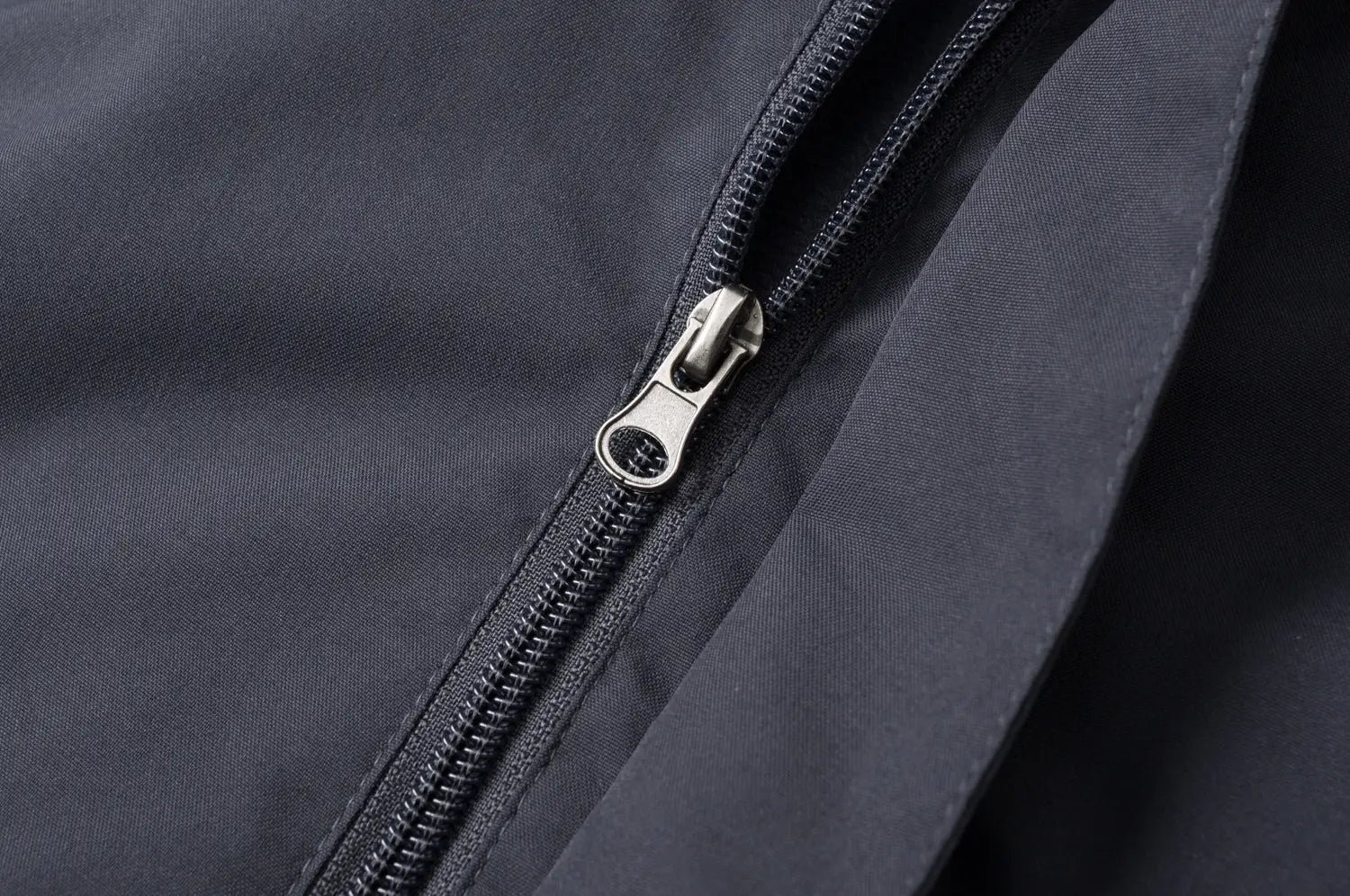 Fermeture éclair ton argent avec une languette de traction minimaliste sur une veste de plein air imperméable à capuche pour hommes et femmes, dans un tissu bleu marine foncé.