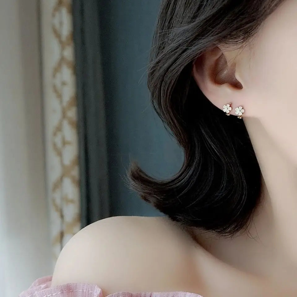Delicate silver four-petal daisy enamel flower clip on and stud earrings adorned with tiny clear crystals.