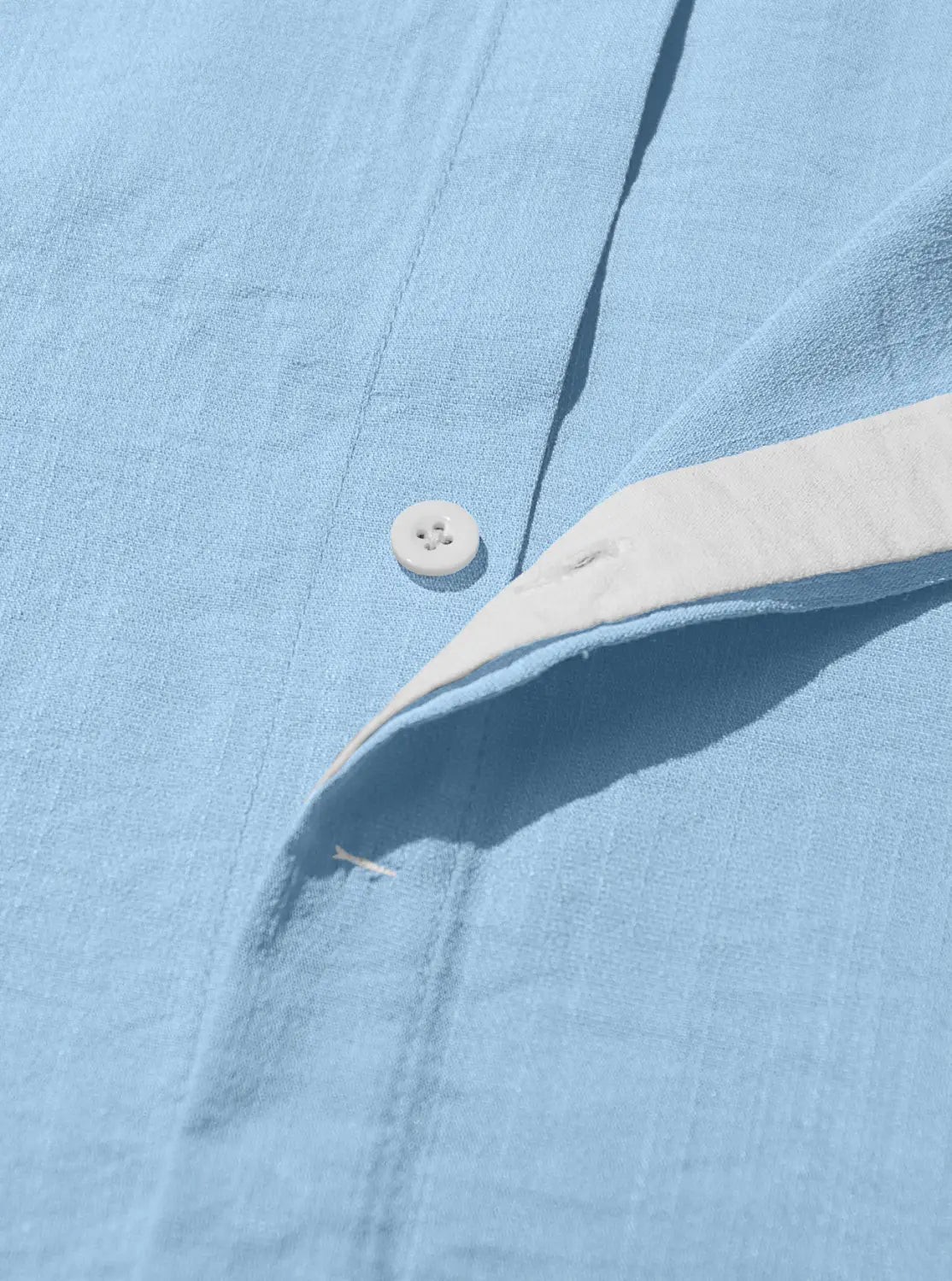 Men’s textured bamboo linen short sleeve button down shirt in light blue with a white button and cream-colored inner collar lining.