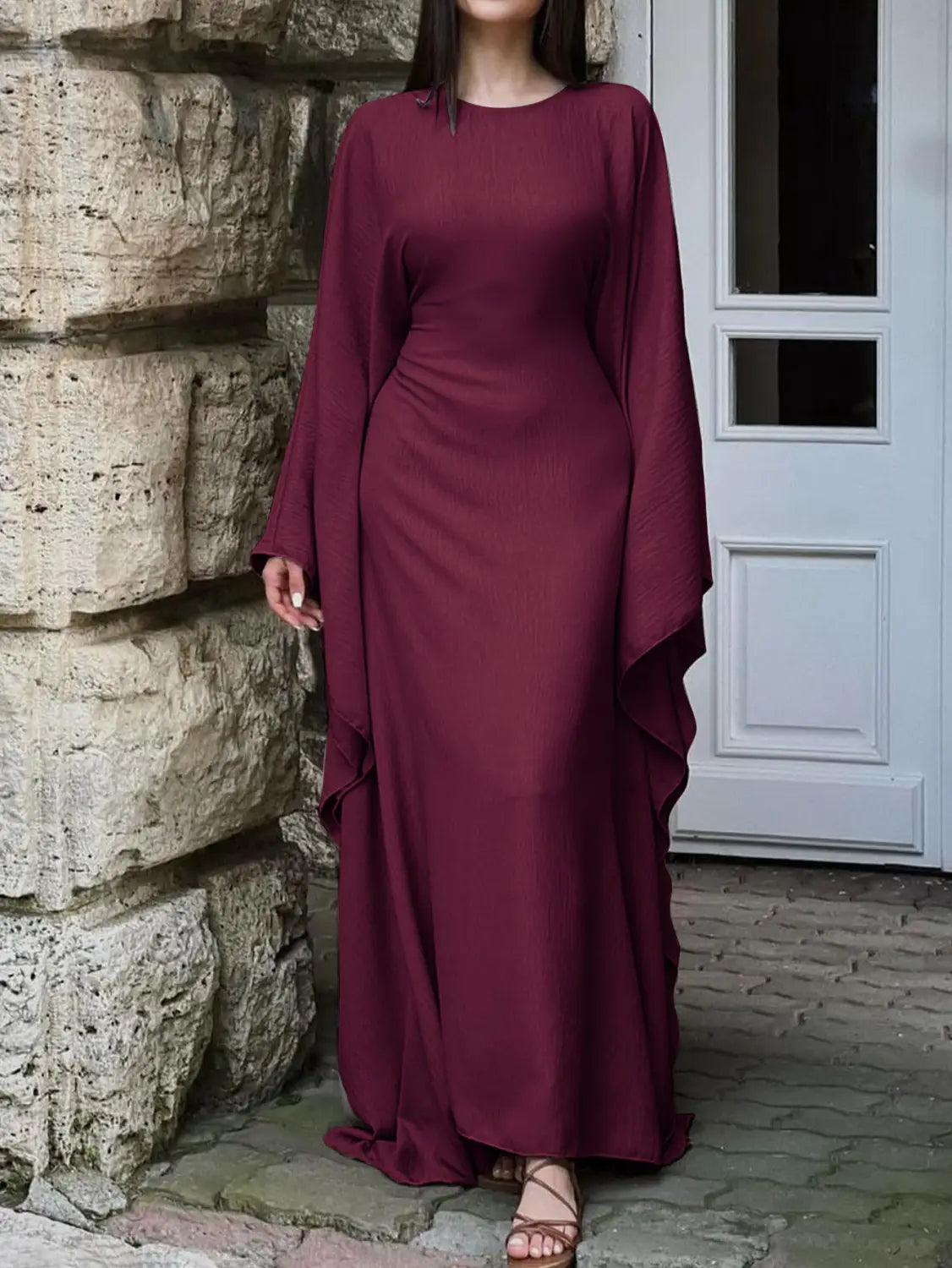 A flowing maroon satin abaya with long wide sleeves and a ruffled hemline designed as an elegant long sleeve satin maxi dress.