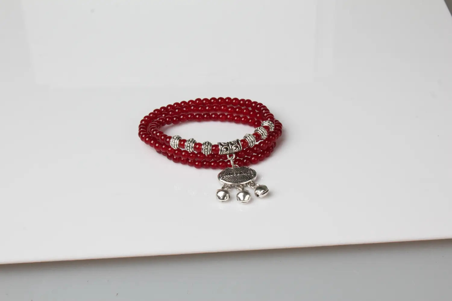 Red agate good luck bracelet featuring red beads with silver-toned metal accents and a dangling charm with three small bells.
