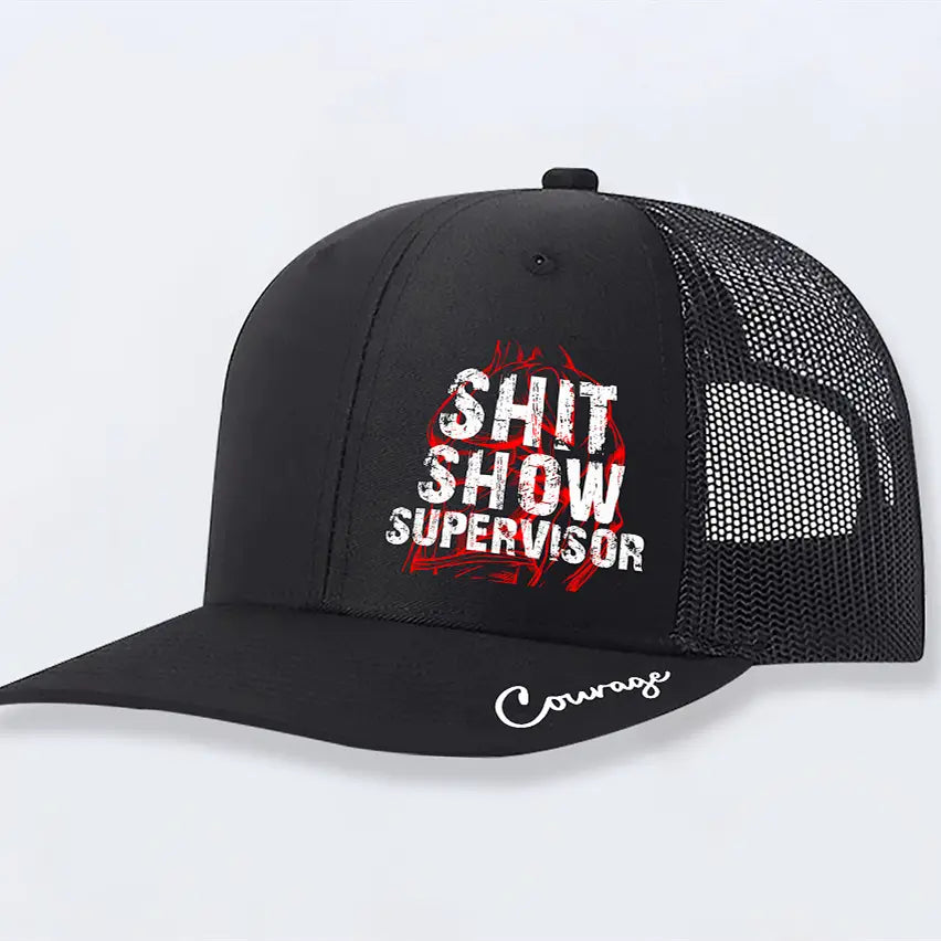 Black trucker hat with mesh back and front panel featuring white and red shit show supervisor text and courage embroidered in cursive on the brim in a shit show supervisor novelty trucker hat for men.