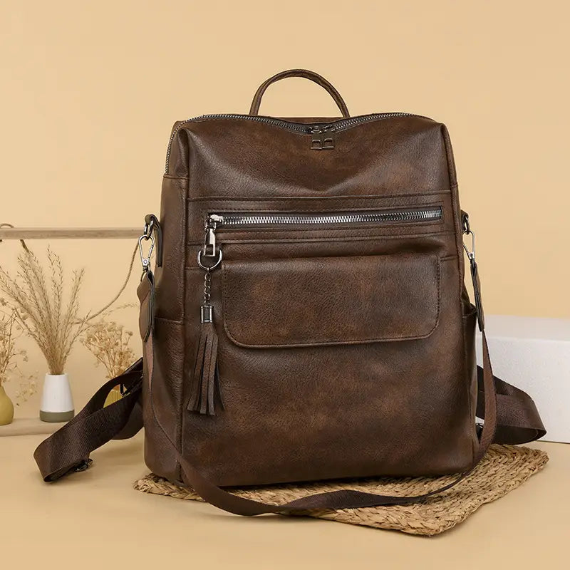 Brown faux leather backpack with front zipper pocket adorned by a tassel and adjustable shoulder straps in one shoulder cream faux leather backpack 35cm style.