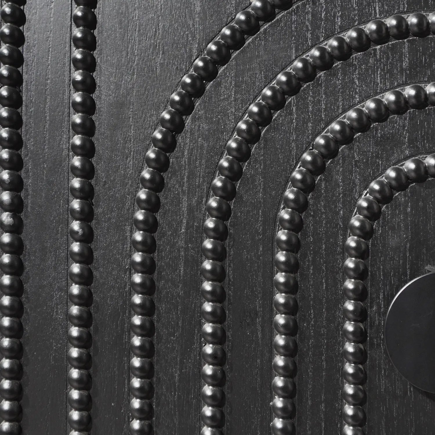 black storage cabinet with arched beaded door featuring a decorative panel of black glossy spherical beads arranged in concentric curved rows on a textured dark wood-like finish.