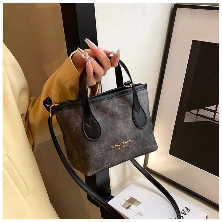 Retro bucket bag textured canvas shoulder handbag in black and gray patterned mini style with black leather handles and a detachable strap featuring gold lettering on the front.