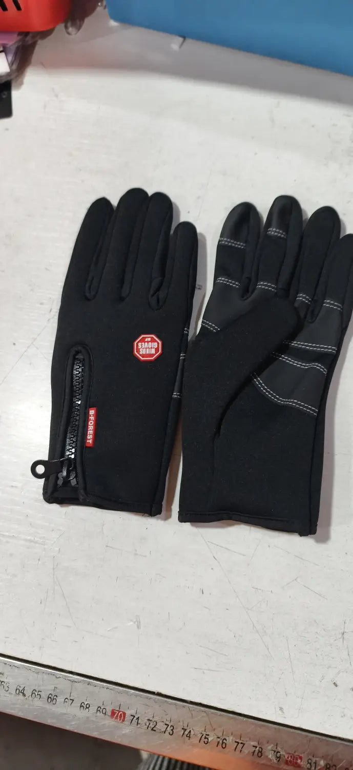 Black windproof touchscreen winter gloves for men and women with gray reinforced panels white stitching and a red logo patch visible on the back side of one hand.