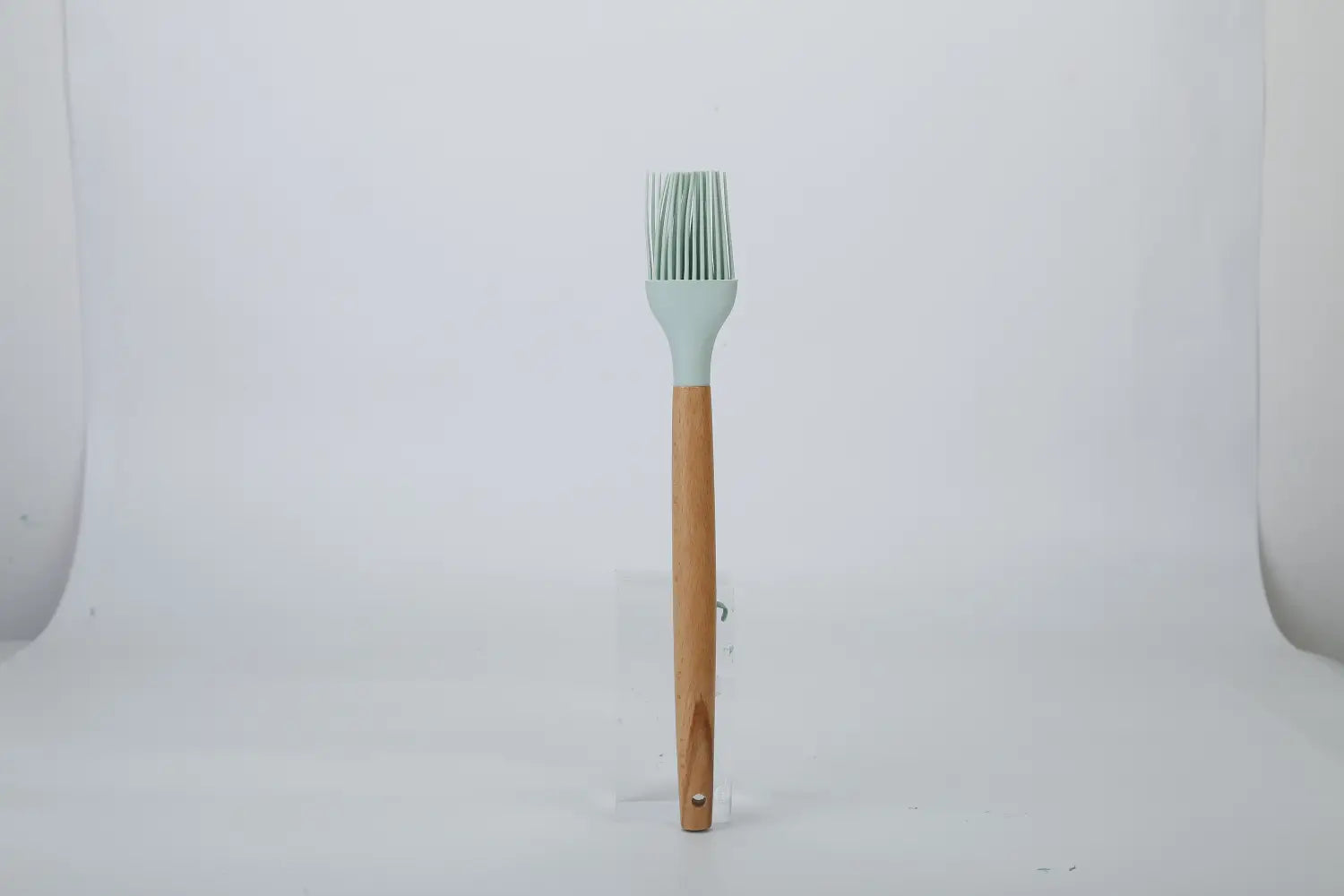 A light green silicone basting brush with a wooden handle from an 11-piece silicone cooking utensil set with wood handles.