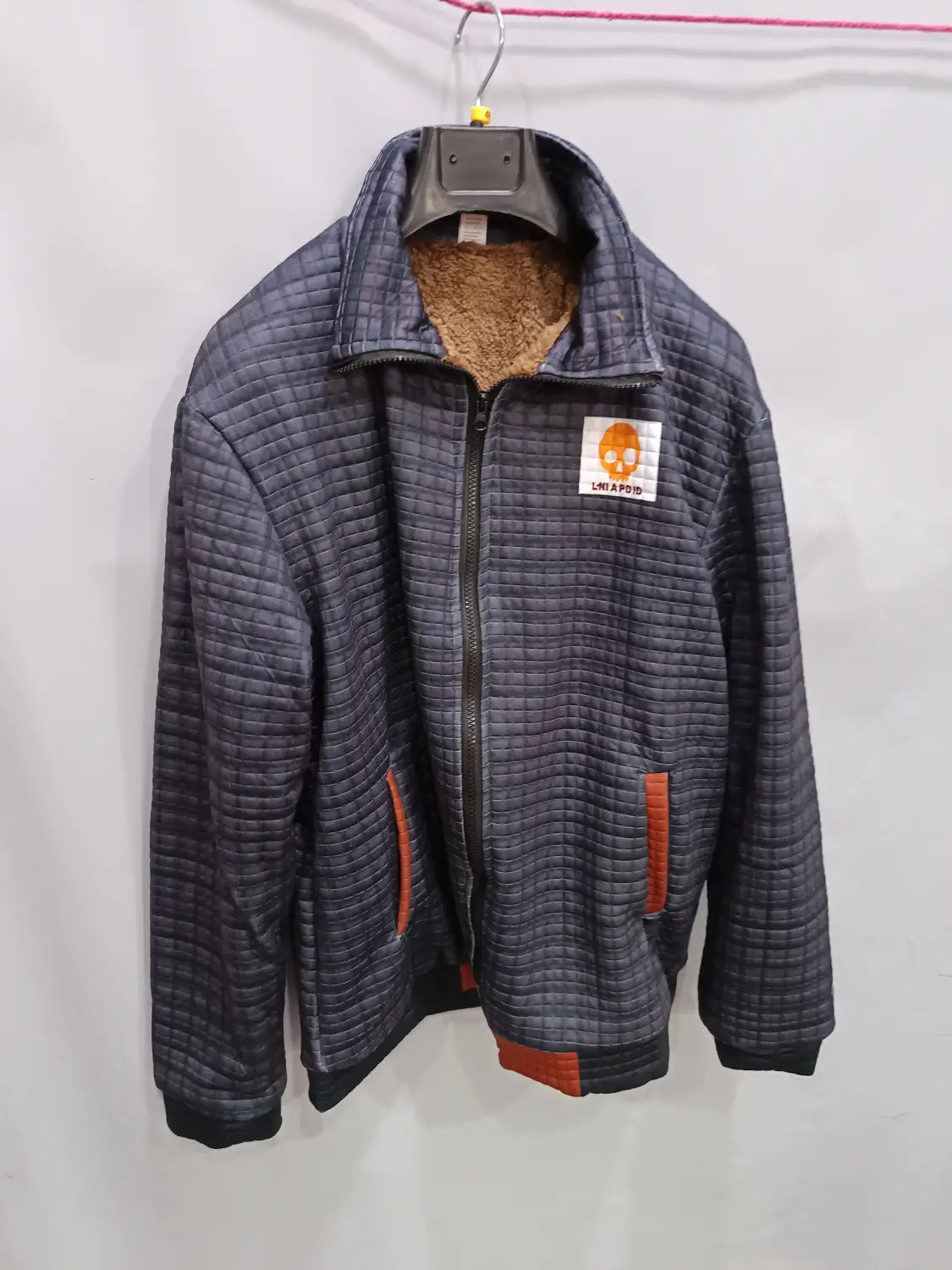 Veste en cuir matelassée doublée en shearling pour homme, en gris foncé, avec des bordures orange sur les poches et les poignets, une doublure en polaire marron moelleuse et une patche logo brodée.