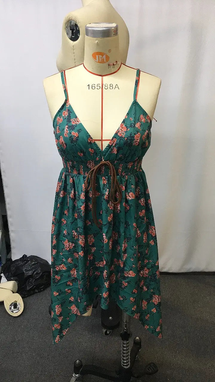 Ein grünes florales Retro-V-Ausschnitt-gesmoktes Mini-Sommerkleid mit dünnen Trägern und einer gebundenen Taille, auf einem Schaufensterpüppchen präsentiert.