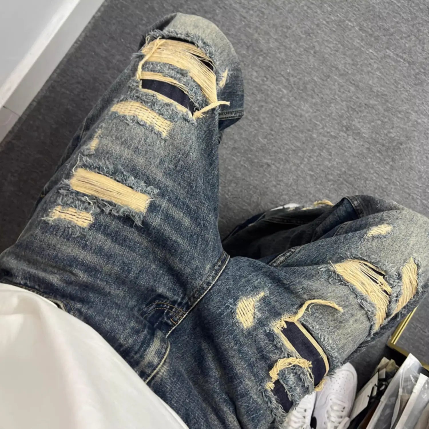 Men’s light blue distressed ripped patch denim jeans featuring prominent yellow frayed patches and detailed rips on blue denim fabric.