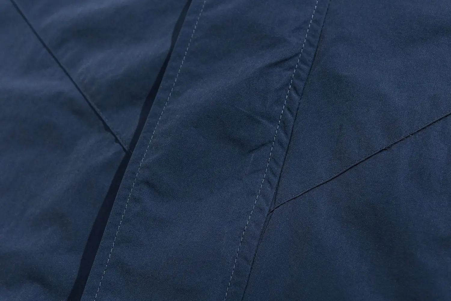 Tissu de veste coupe-vent ample bleu marine foncé à blocs de couleurs brodés, avec un discret piquage diagonal et une surface lisse légèrement texturée.