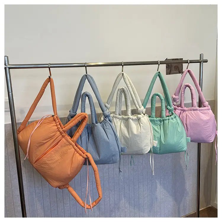 A collection of pastel-colored quilted puffer tote bags in orange blue white mint green and pink made of lightweight nylon suitable for use as shoulder bags.