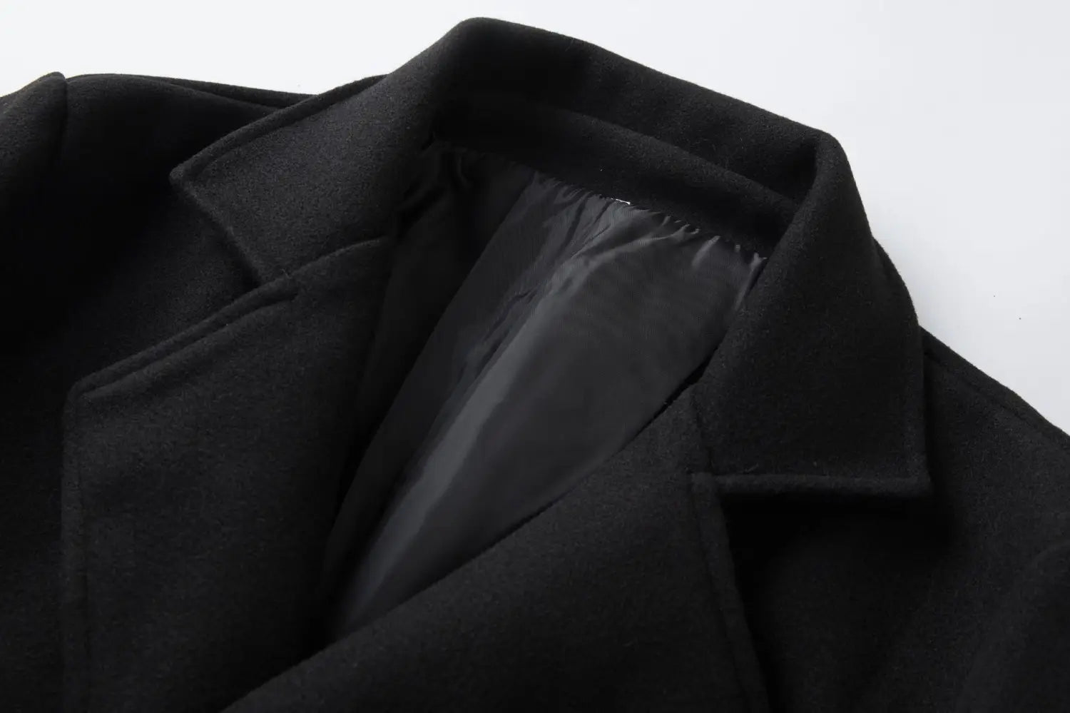 Black wool double breasted mid length men’s overcoat with structured collar and smooth matte finish.