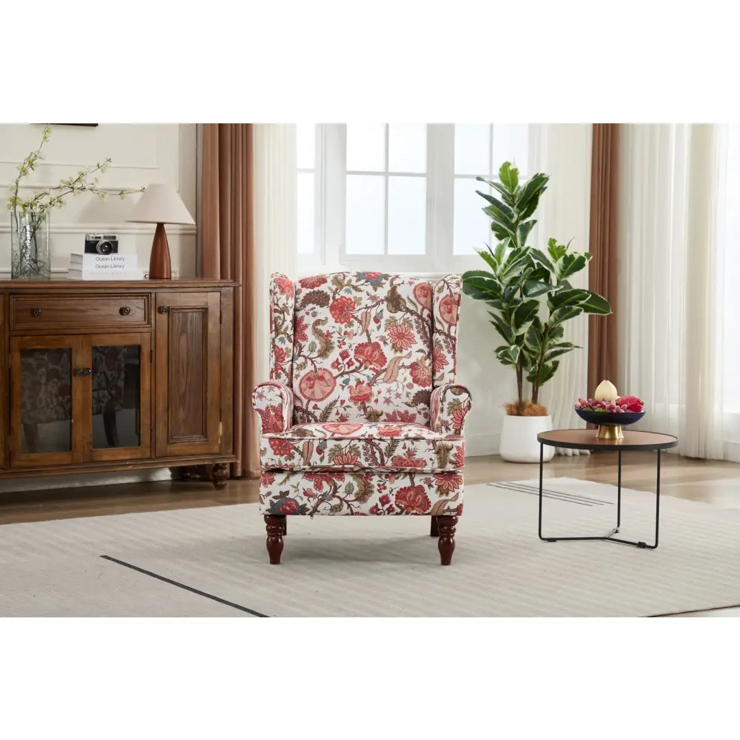 Una silla tipo ala con respaldo capitoné floral, tapizada en un tejido suave color crema con diseños botánicos rojos y verdes vibrantes y patas de madera retro.