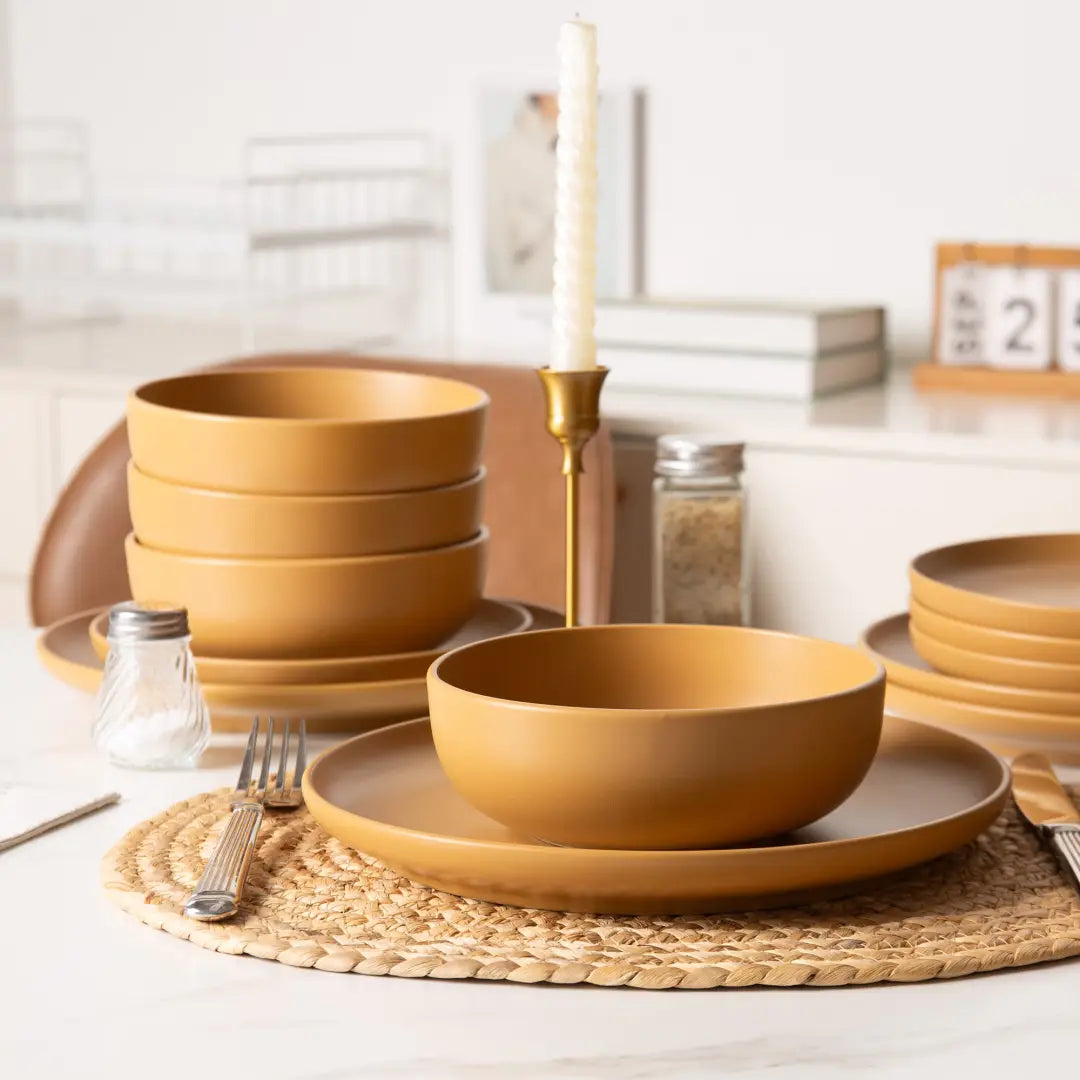 Set of matte mustard-yellow stoneware ceramic bowls and plates from a 12 piece dinnerware set for four arranged on a woven placemat.