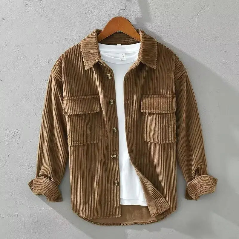 Ein braunes, schmal geschnittenes Cordhemd für Herren mit langem Ärmel, klassischem Kragen und zwei vorderen Taschen, das an einem Holzkleiderbügel hängt und sich für Herbstbekleidung eignet.