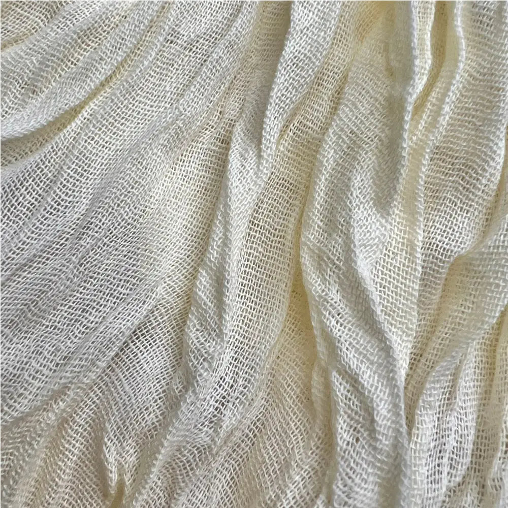 Ein off-white, locker gewebter weißer Crinkle-Schal mit einem texturierten, atmungsaktiven Mesh-Muster, ideal als Sommeraccessoire.