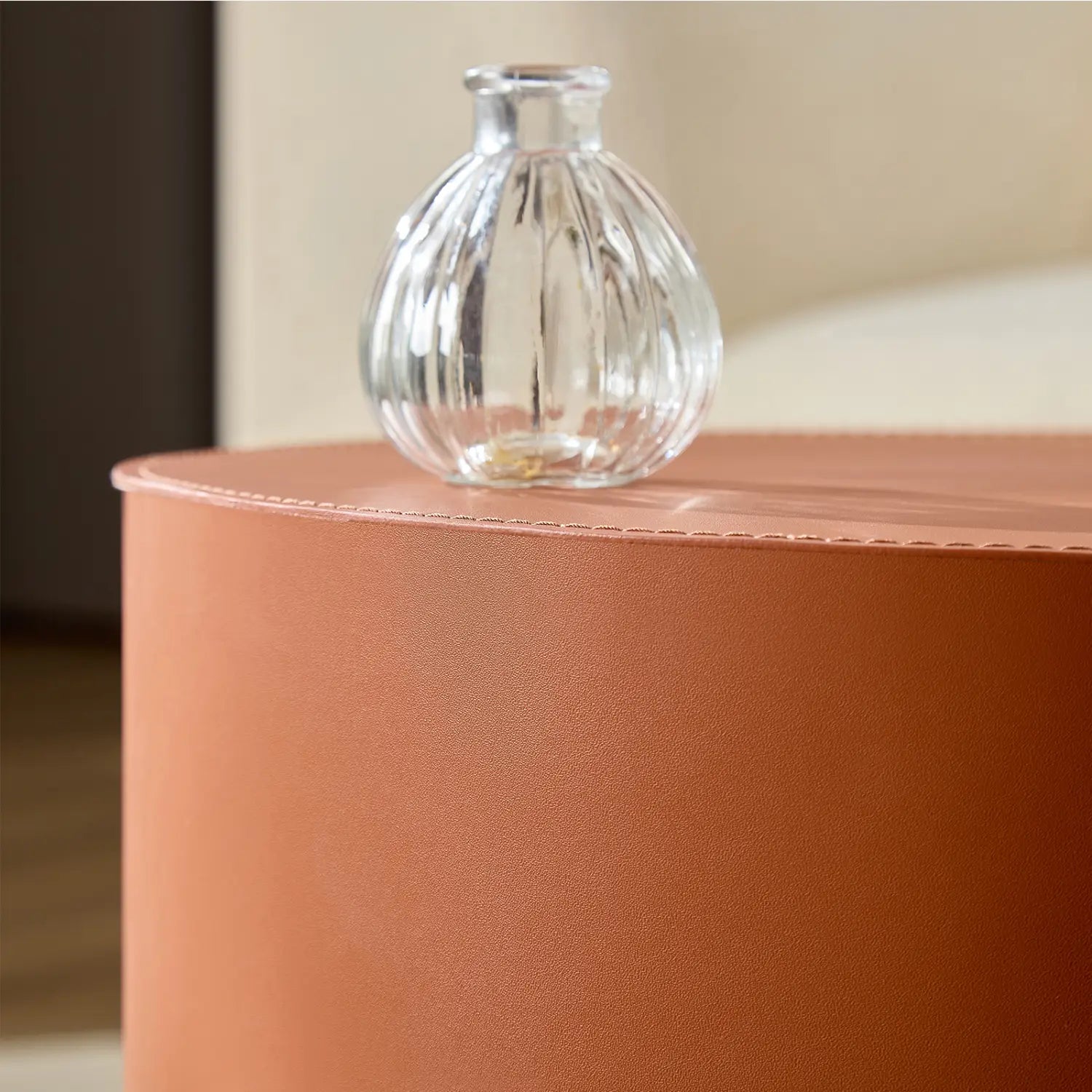 Jarrón de vidrio transparente con textura acanalada vertical, mostrado junto con un conjunto de mesa de centro redonda de cuero de silla color naranja