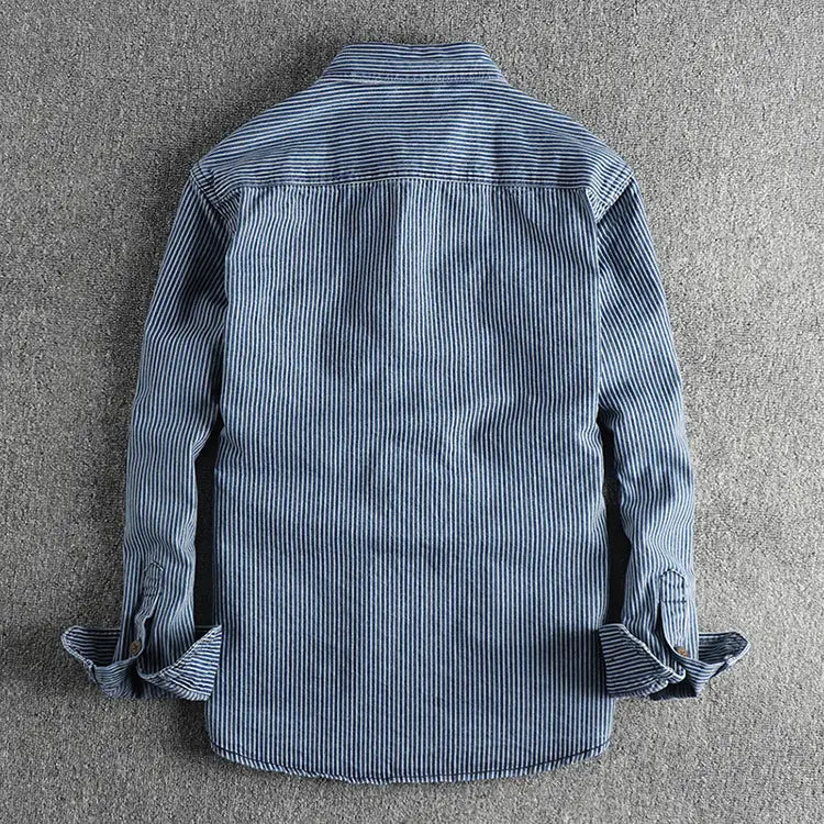 Striped denim shirt for men featuring blue and white vertically striped long-sleeved button-up design with rolled cuffs.