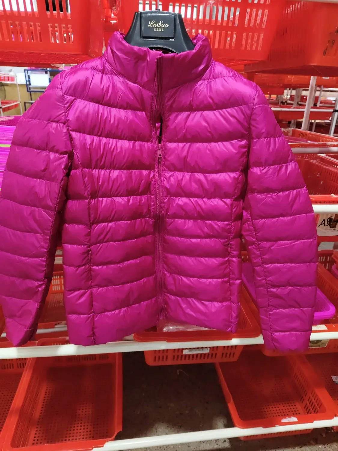 Eine kräftige Magentafarbene Slim-Down-Steppjacke mit Steppdesign und Stehkragen, die auf einem schwarzen Bügel präsentiert wird.