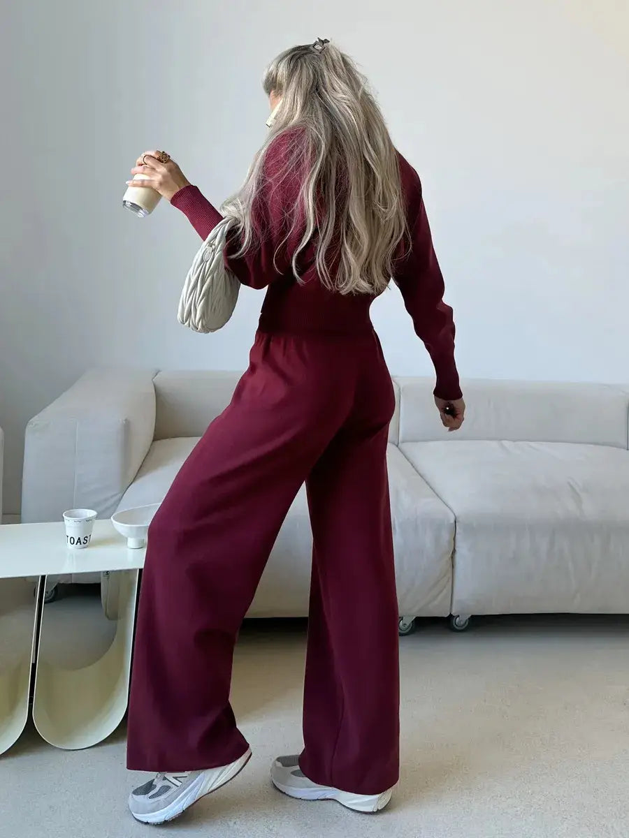 A maroon women’s knit zip up cardigan and wide leg pant set featuring a long-sleeved relaxed fit jumpsuit with wide-leg pants.