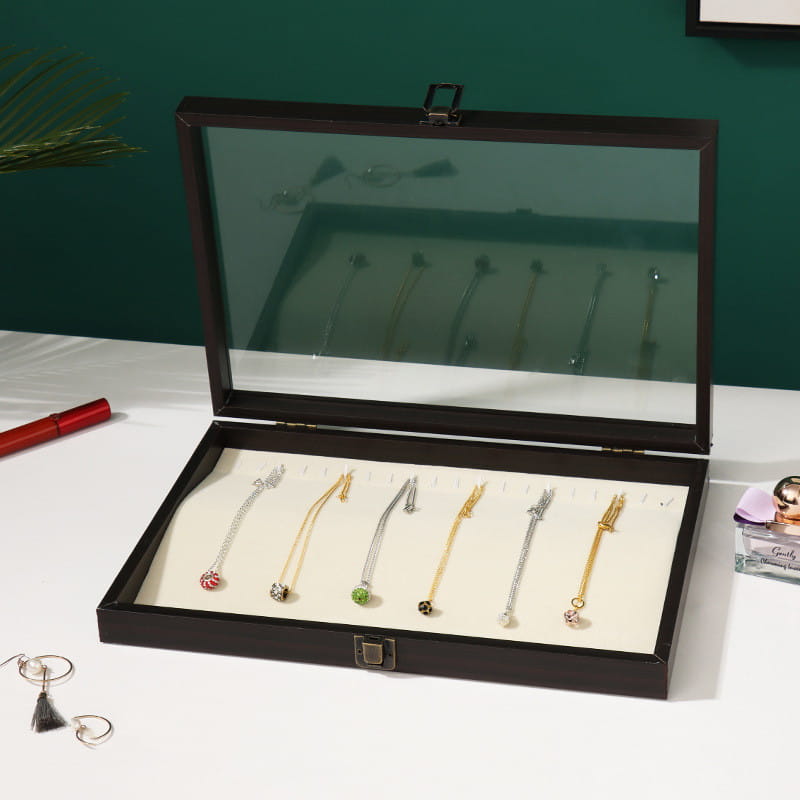 Rosewood jewelry display box with glass lid and silver-toned metal clasps in black wood showcasing six necklaces on white foam inserts.