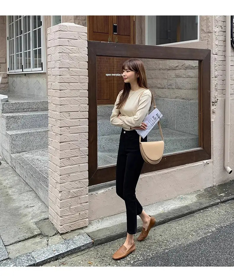 Beige Ledertasche für die Schulter über Kreuz mit minimalistischem Design und sanft geschwungener Form, kombiniert mit schwarzen Samtgefütterten High-Waist-Jeans-Leggings.