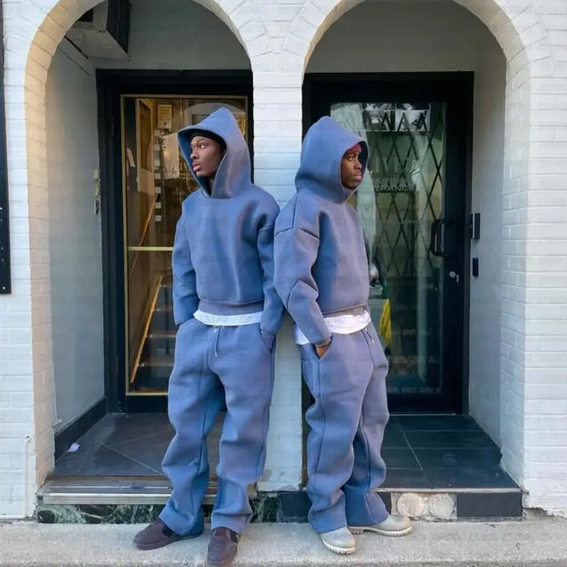 Deux personnes portant l’ensemble oversize unisexe streetwear assorti, composé d’un sweat à capuche et d’un pantalon de survêtement, couleur bleu ardoise, avec des ceintures blanches, conçu pour un confort d’usage courant.