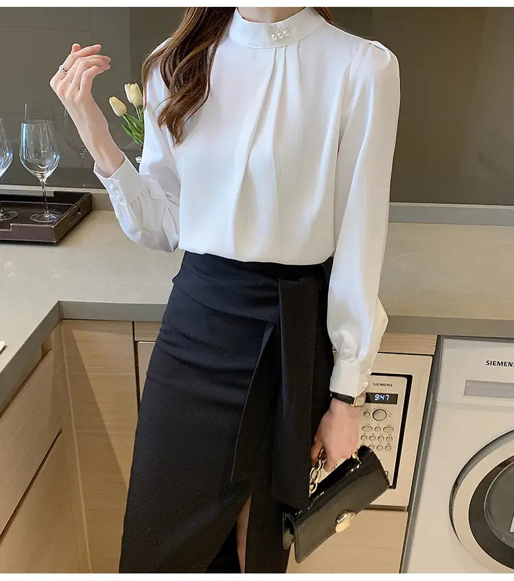 Blouse en satin blanche pour femmes, avec un col haut et des accents de boutons perle au niveau de l’encolure.
