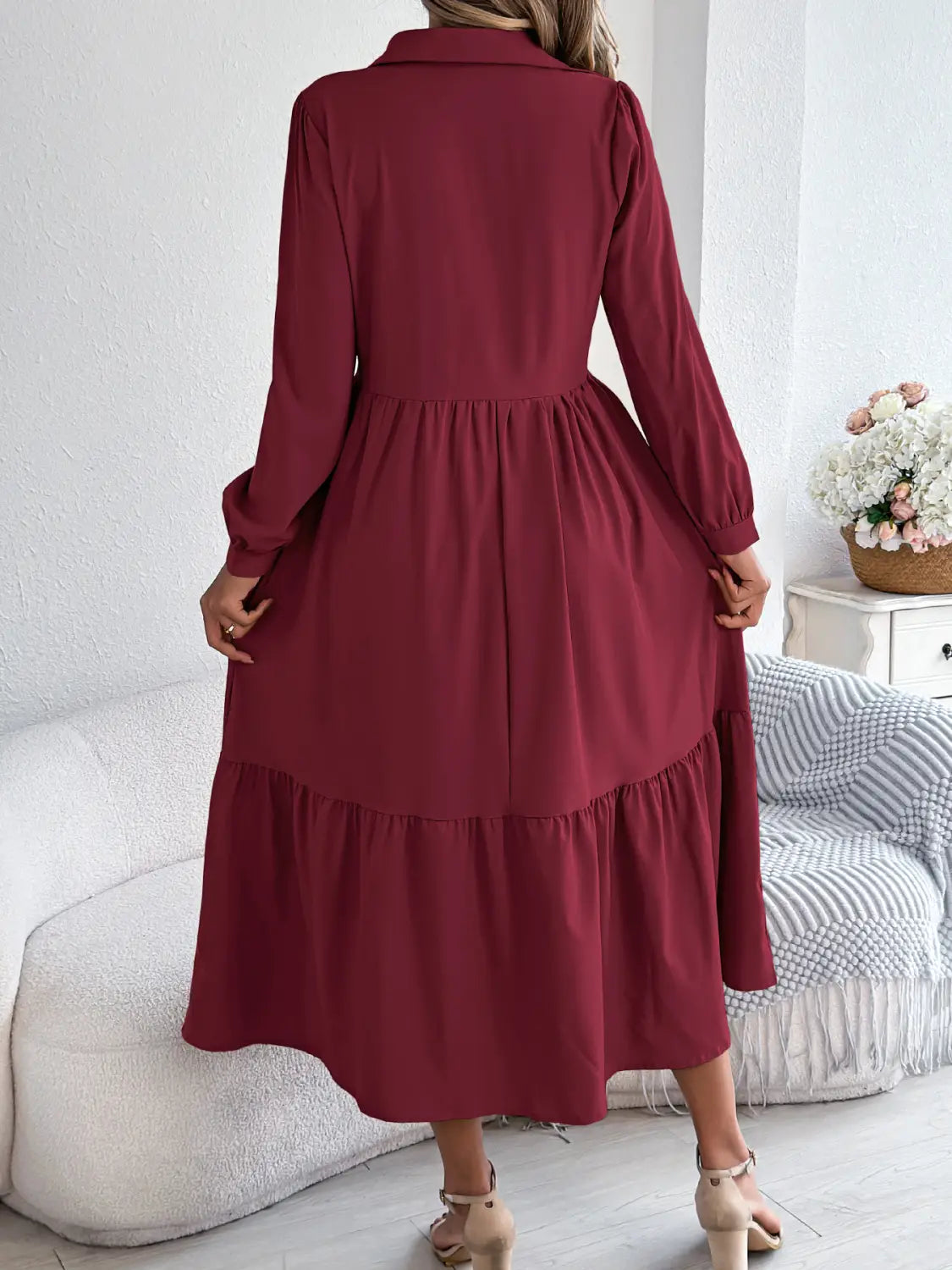 A woman wears a long sleeve burgundy tiered button down midi dress with a collar and gathered waist.