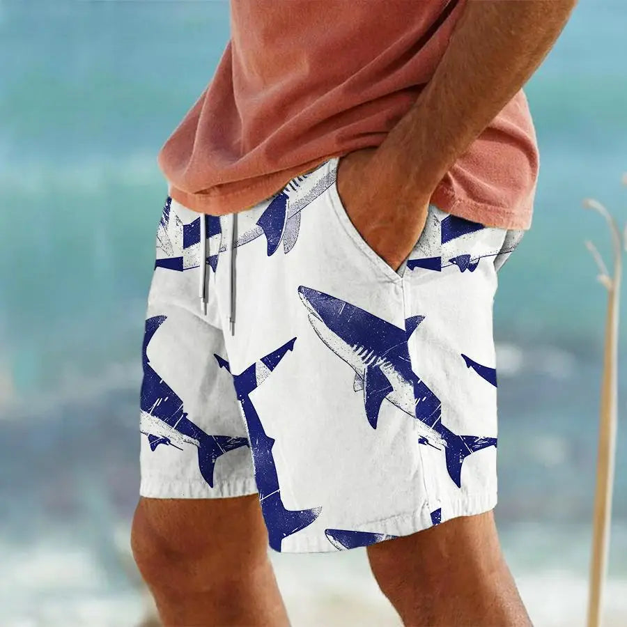 Men’s white swim trunks with a bold navy blue shark pattern featuring a distressed graphic design and a striped tropical print.