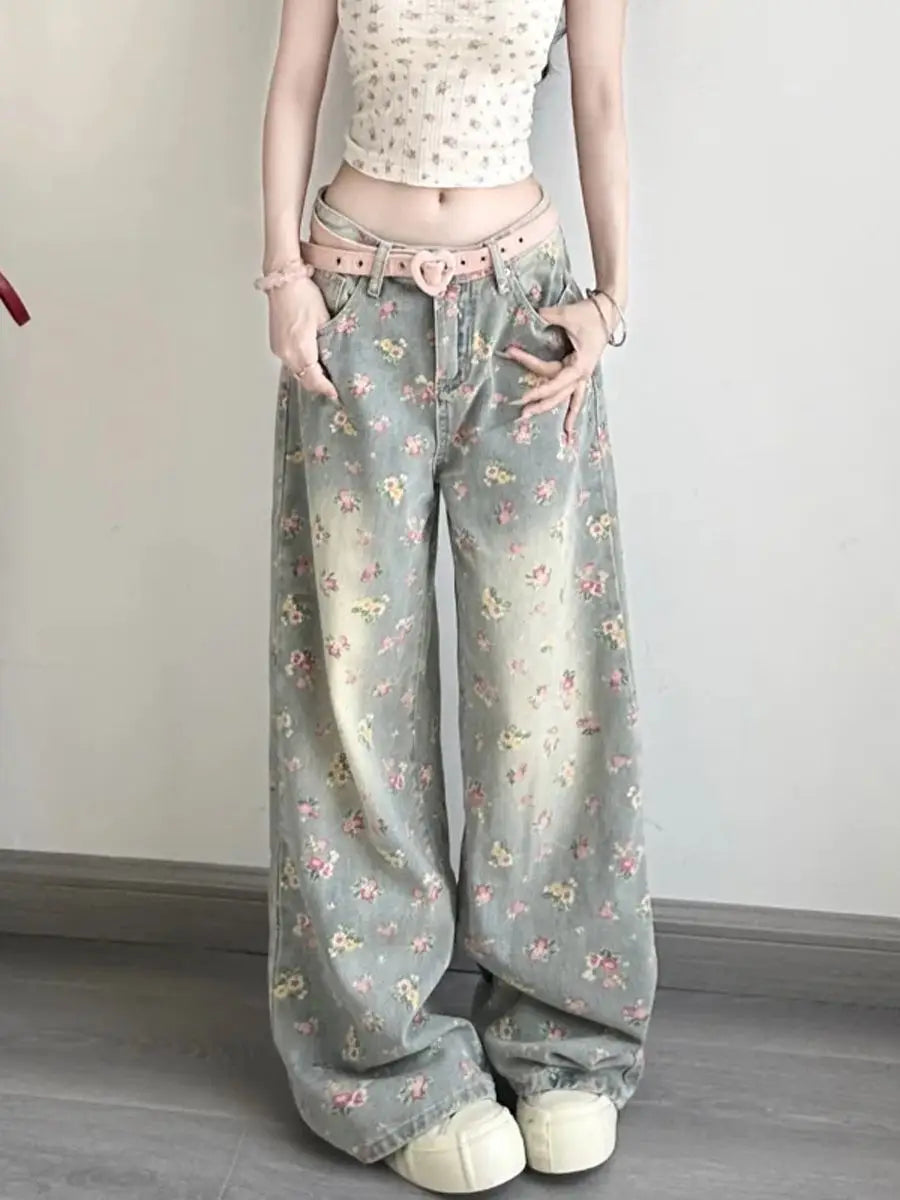 Floral high waist wide leg denim jeans featuring a faded green base with delicate pink and yellow floral pattern and a light pink belt cinching the waist.