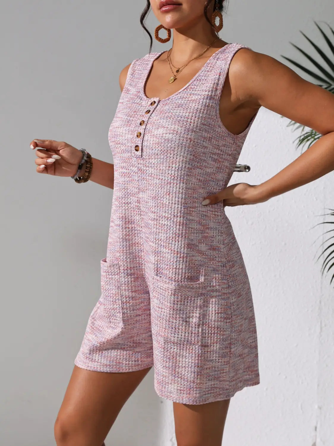 A pink waffle knit sleeveless romper with a button-front neckline and side pockets.