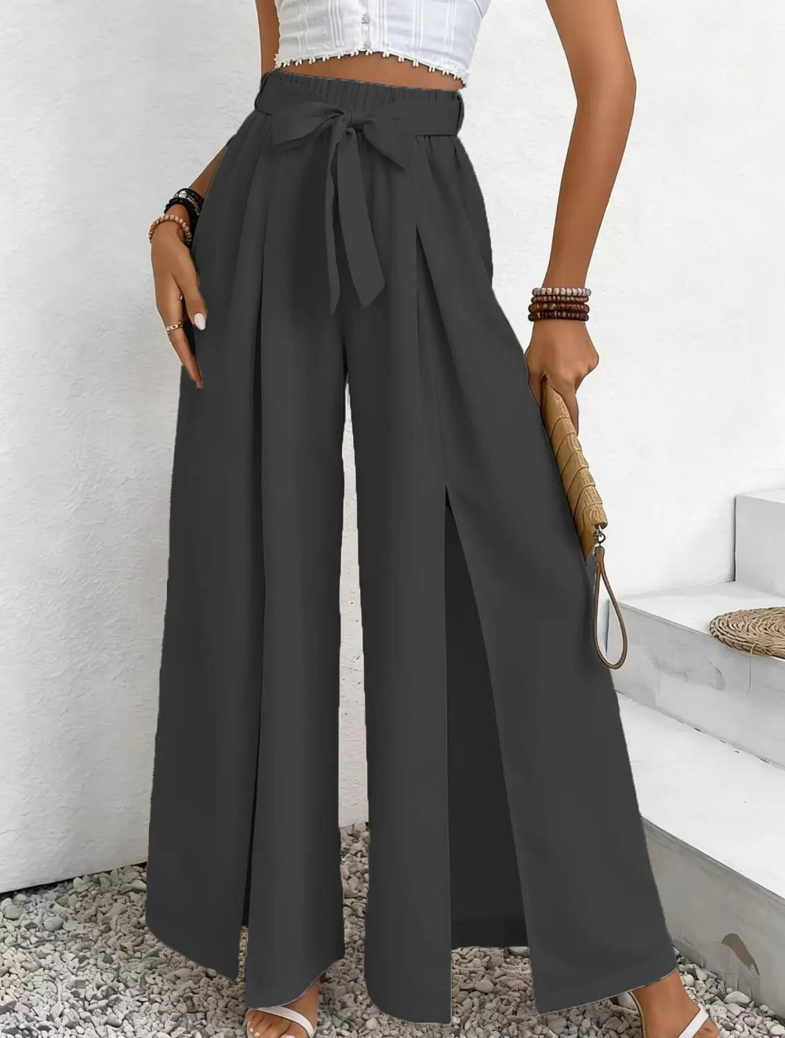 Pantalon ample à taille haute gris foncé, avec une ceinture nouée et des fentes latérales, conçu comme un pantalon ample et décontracté.