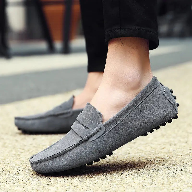Mocassins en daim classiques en gris, avec surpiqûres contrastées, une bride cousue et des semelles crantées en caoutchouc noir.