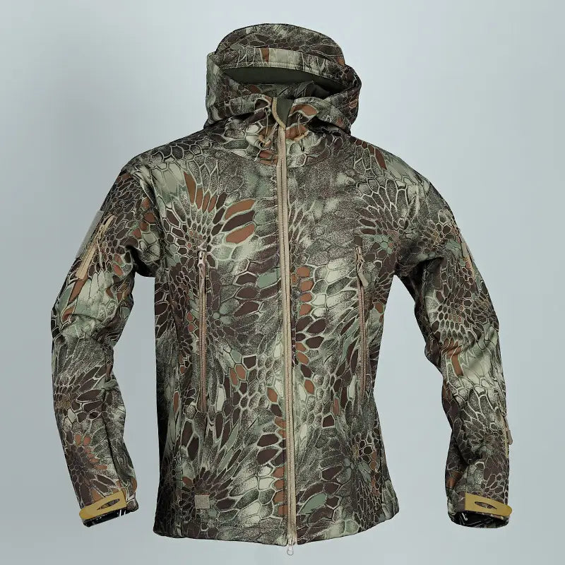 Une veste tactique softshell à capuche, avec un motif camouflage détaillé à plusieurs tonalités, comprenant des nuances de brun, vert et gris, conçue pour un usage extérieur.
