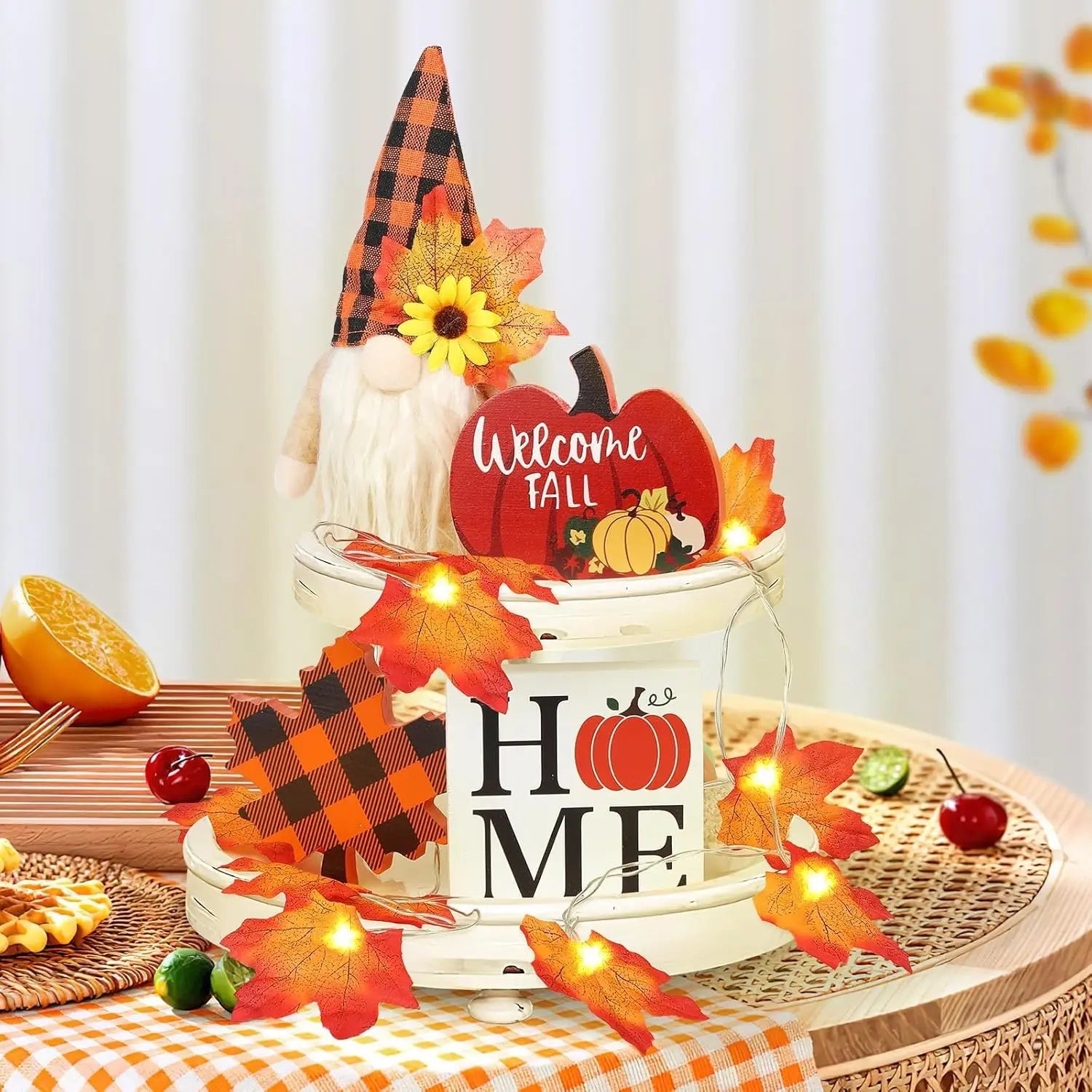 white ceramic bucket with home and pumpkin design adorned with autumn leaves string lights and a gnome figurine wearing an orange plaid hat in fall tiered tray decor set with gnomes and lights