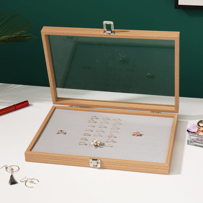 Rosewood jewelry display box with a light wood frame, clear glass lid, silver-toned latches, and soft gray interior showcasing rings.