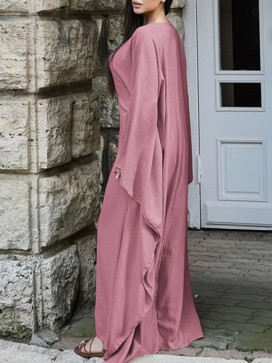 A flowing dusty rose-colored satin maxi dress with long wide sleeves and a draped asymmetrical ruffled hem.